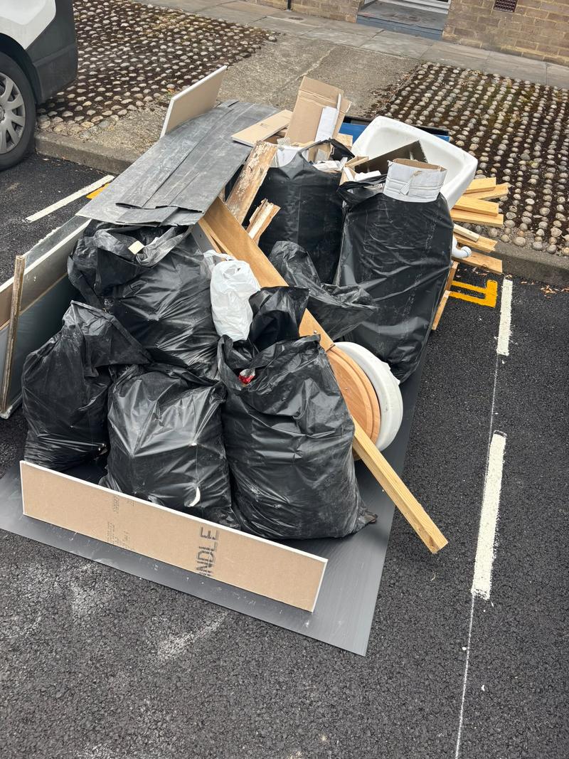 Bagged waste, timber, panels and sanitaryware in a parking space before clearance