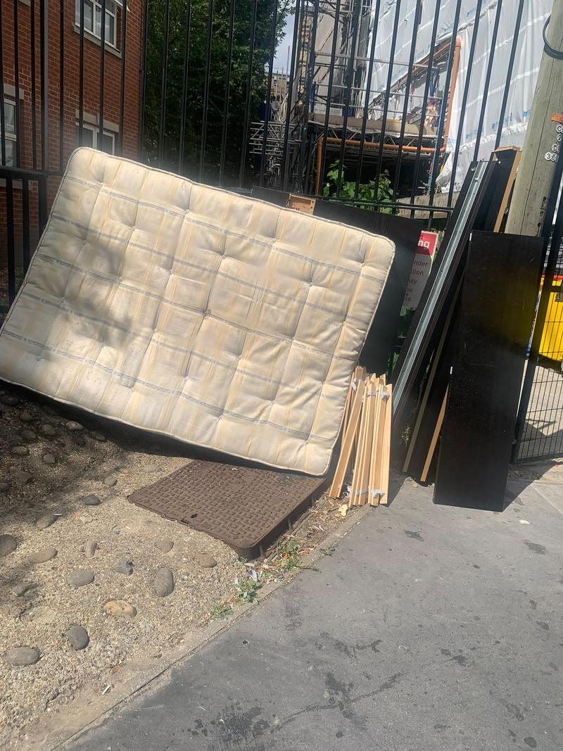 Mattress and furniture panels piled against a metal fence before clearance