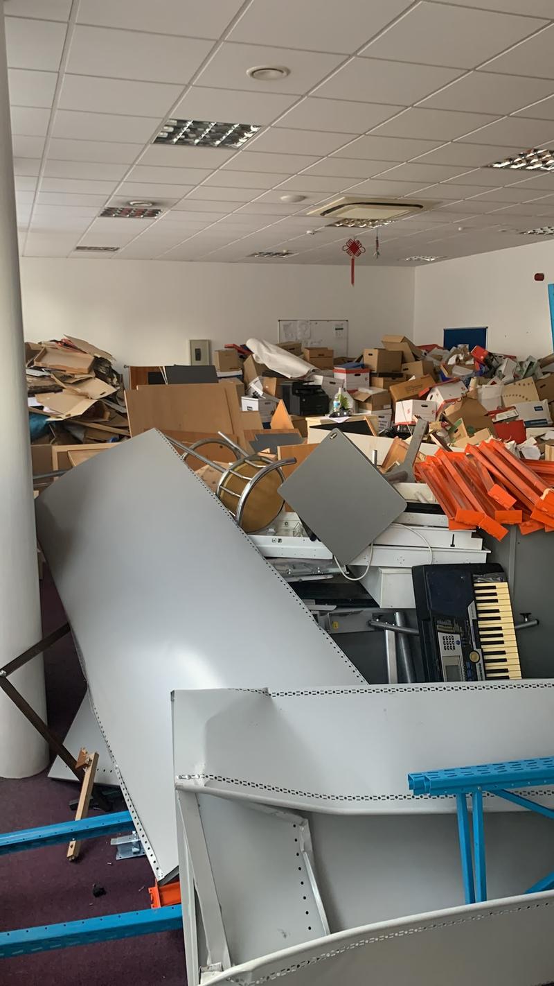 Office interior filled with shelving, furniture, cardboard and loose contents before clearance